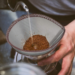 Finmaskigt kaffefilter under manuell kaffebryggning med varmt vatten och malet kaffe