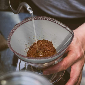 V-format återanvändbart kaffefilter i rostfritt stål under pour-over-bryggning, med vatten som hälls över malet kaffe